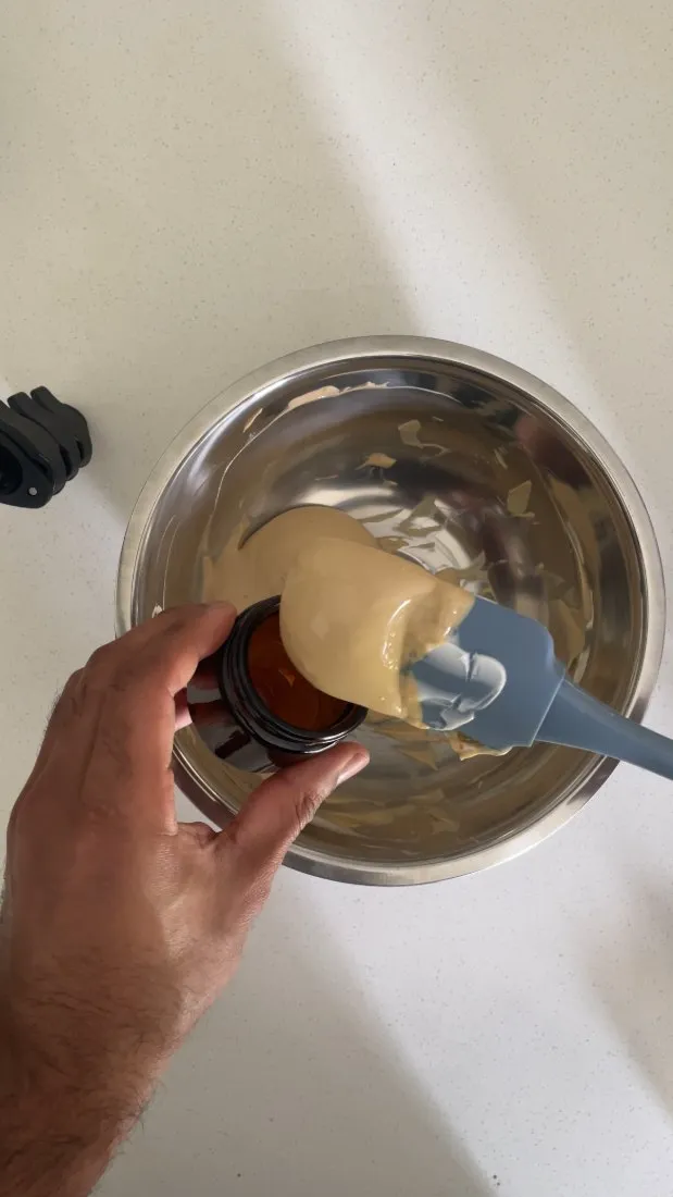 A finished herbal skin cream being potted into an amber jar